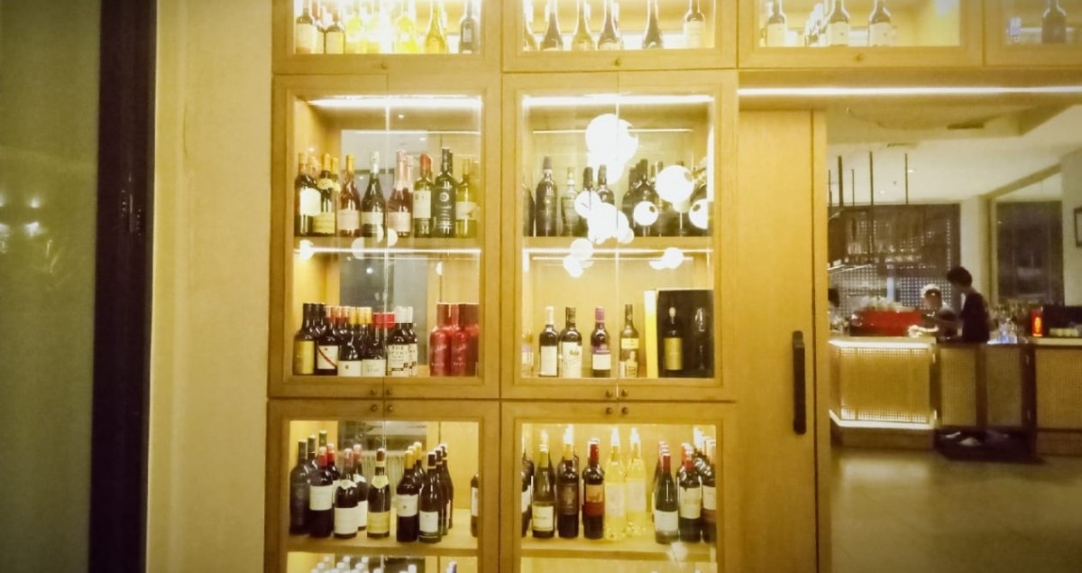 Koleksi wine di Slide Bar ini diletakkan di rak kaca dekat pintu menuju area outdoor